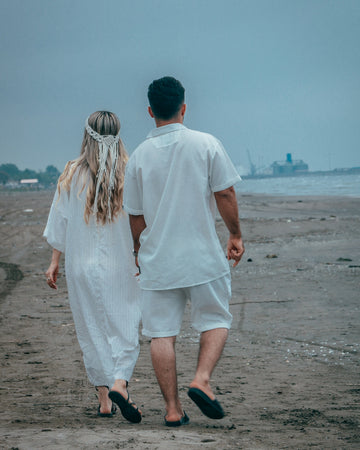 Two people in white walking on a sandy beach.