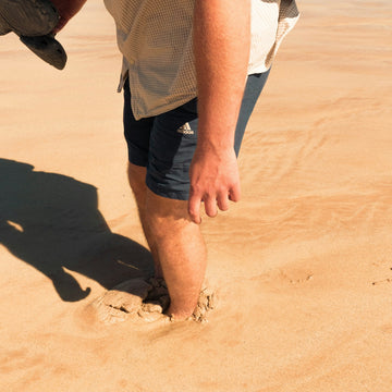 A person's legs sinking into soft sand on a beach.