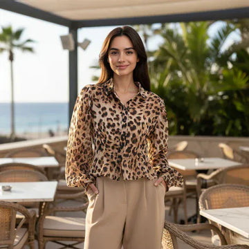 Woman wearing a leopard print blouse standing in an outdoor setting with tables and chairs.